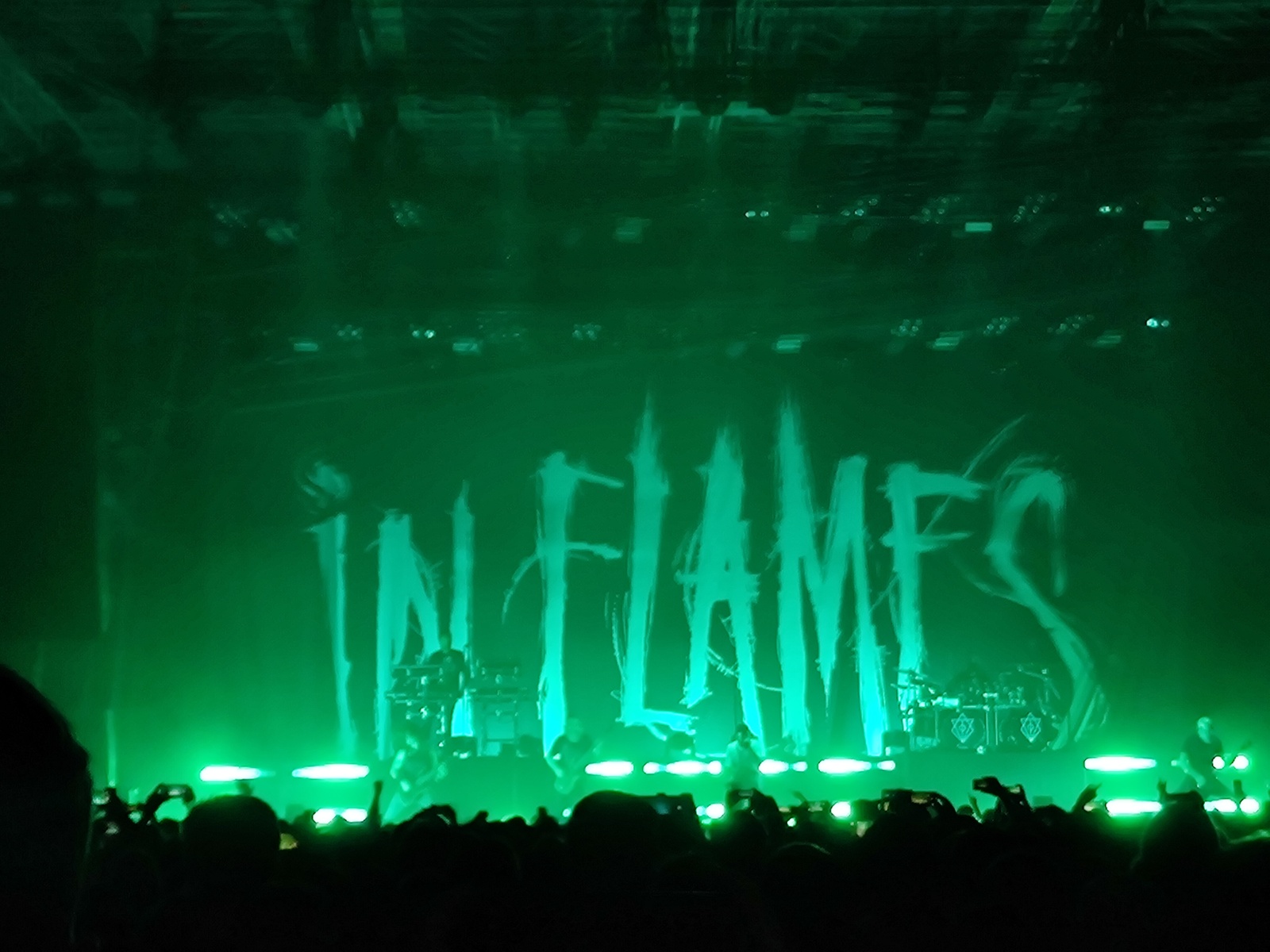 Greenly lit concert stage from some distance. The In Flames text logo is written across the back of the stage.